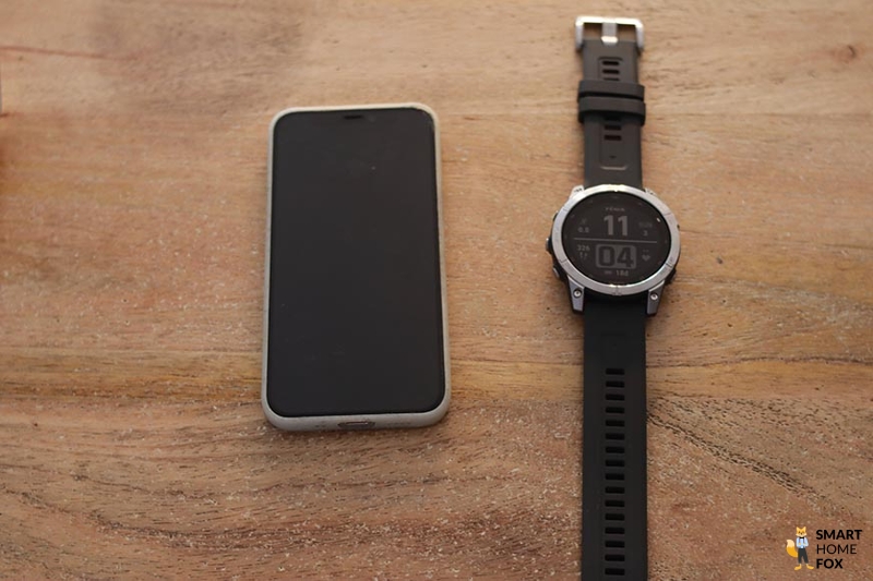 Man sieht die Garmin Fenix 7 neben einem Handy auf einem Tisch liegen.